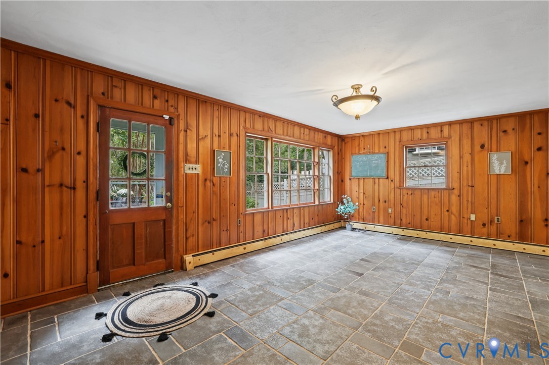 Wood-paneled wall treatment, stone flooring, multi-pane glass entrance door, and multi-pane window  and door to patio