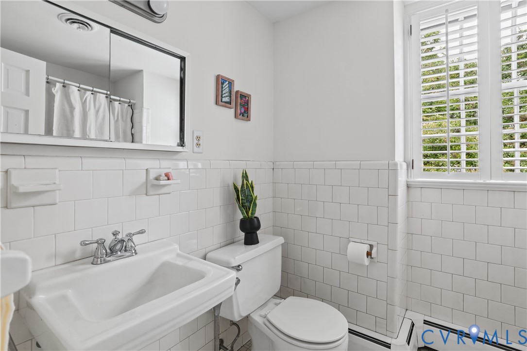 Wall-mounted medicine cabinet with a mirror, porcelain wall-mounted sink with chrome dual-handle faucet, white subway tile wainscoting, and shuttered windows