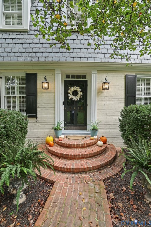 Exterior facade featuring painted brick, classic dark shutters, multi-pane windows, a dark glass-panel front door with transom light, and circular brick entry steps