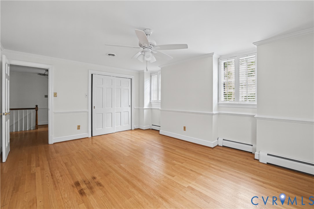 Interior room featuring wood-finish flooring, chair rail molding, a white ceiling fan with integrated lighting, dual-pane windows with plantation shutters, and a sliding door closet
