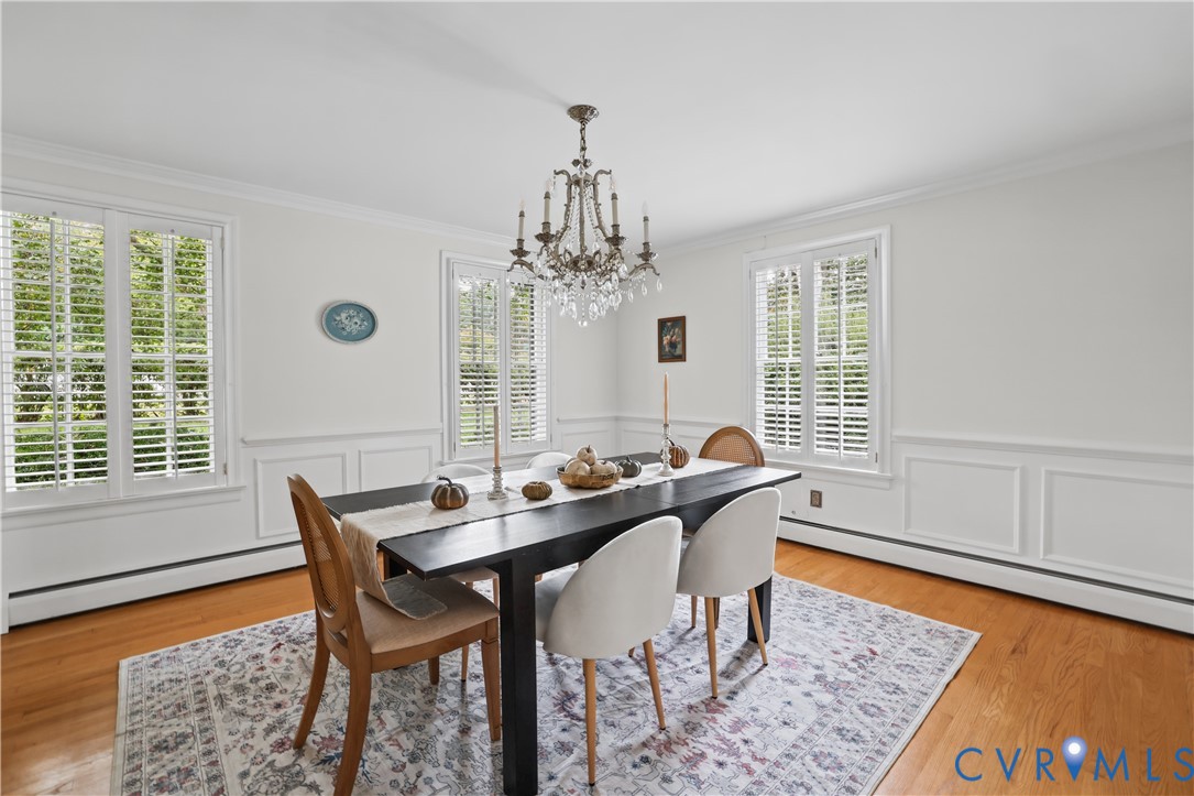 Hardwood flooring, wainscoting, white plantation shutters, and a crystal chandelier