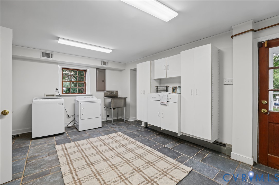 Laundry area featuring stone-finish tile flooring, white built-in cabinetry, stainless steel utility sink, and a glass-paneled exterior door