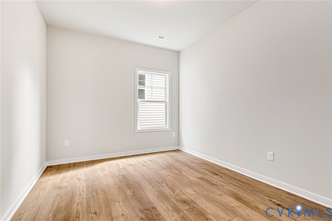 Light-filled room featuring wood-finish flooring, neutral wall paint, white trim, and a window with horizontal blinds