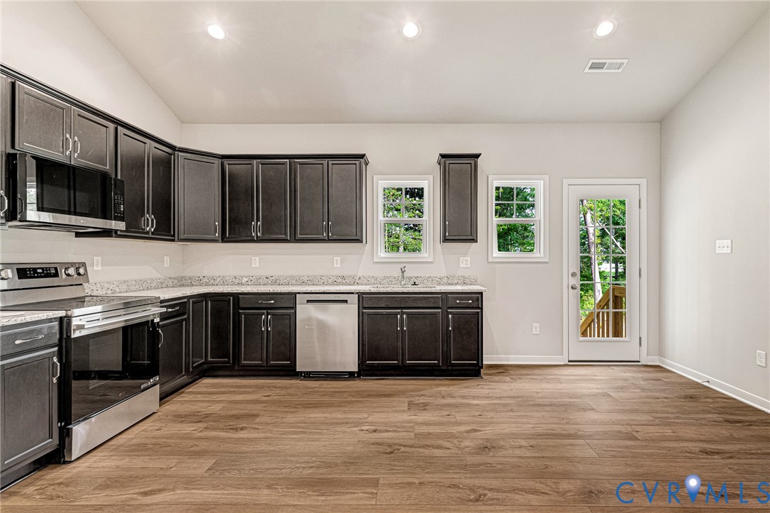 Open-concept kitchen featuring dark wood cabinetry, light-toned countertops, wood-finish flooring, stainless steel appliances, and recessed lighting