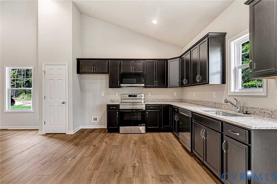 Kitchen featuring wood-finish flooring, dark cabinetry, light-colored countertops, stainless steel appliances, and a vaulted ceiling