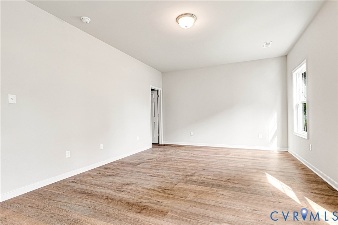 Spacious room featuring wood-finish flooring, white baseboards, and neutral wall paint