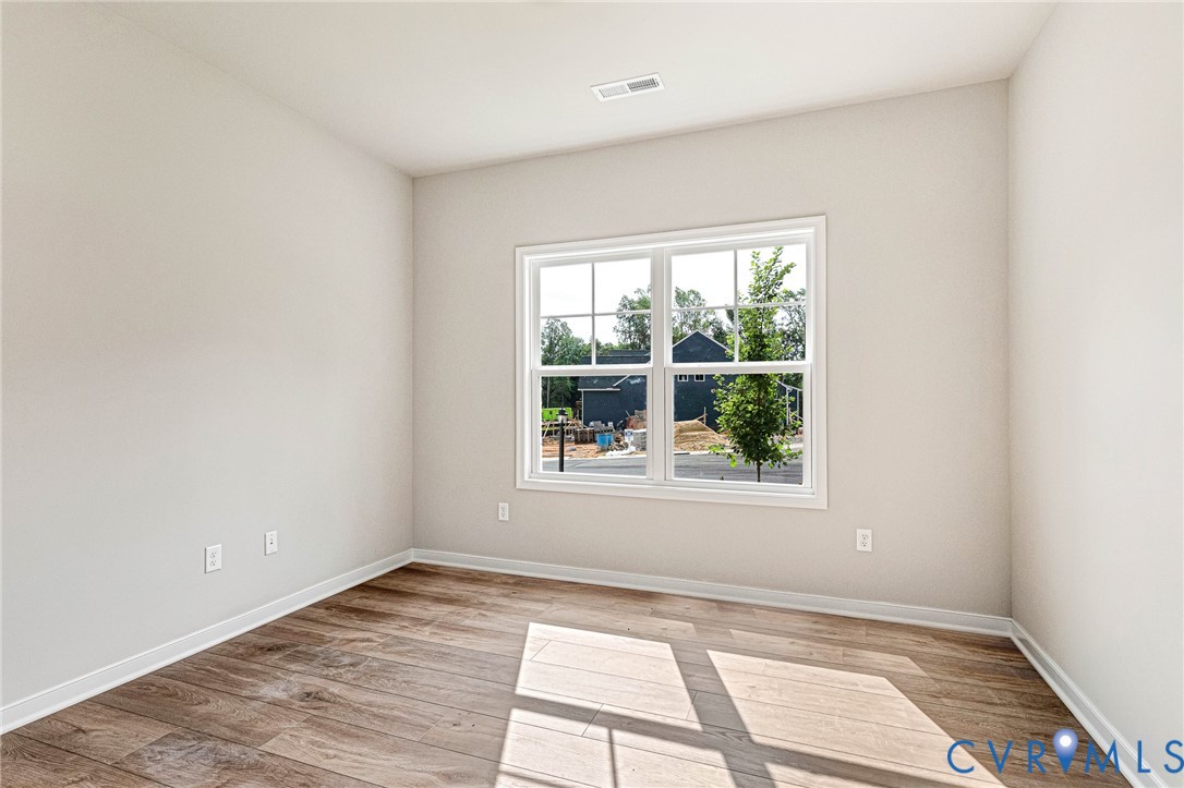 Room featuring a large white-framed window, wood-finish flooring, light neutral-toned walls, white baseboards, and a ceiling vent