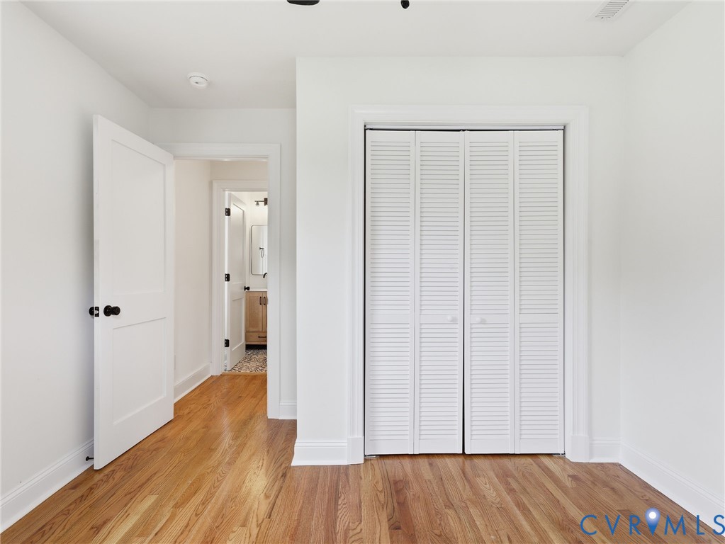 Bedroom featuring wood-finish flooring, white walls, and a bi-fold louvered closet door