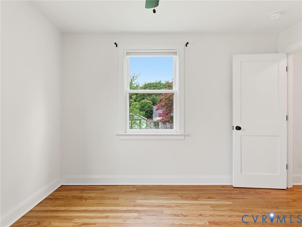 Bright room featuring wood-finish flooring, white walls, and a single window with white trim