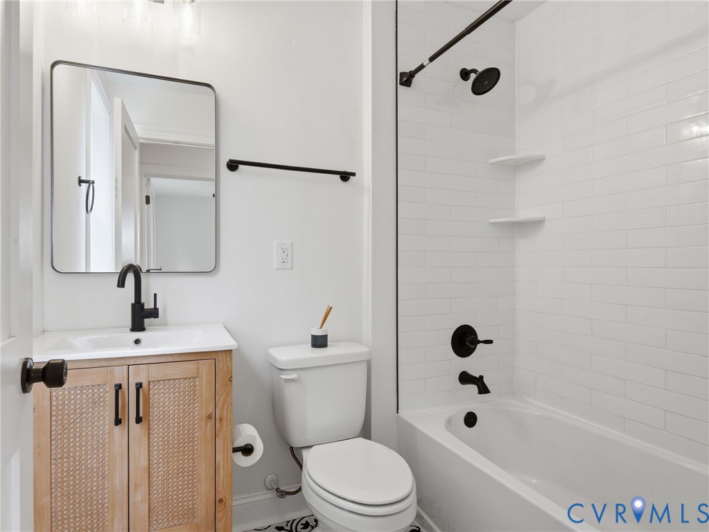 Bathroom featuring a light wood-finish vanity with a rectangular sink, black fixtures, a framed mirror, and a full-size bathtub with white subway tile surround and black shower fixtures