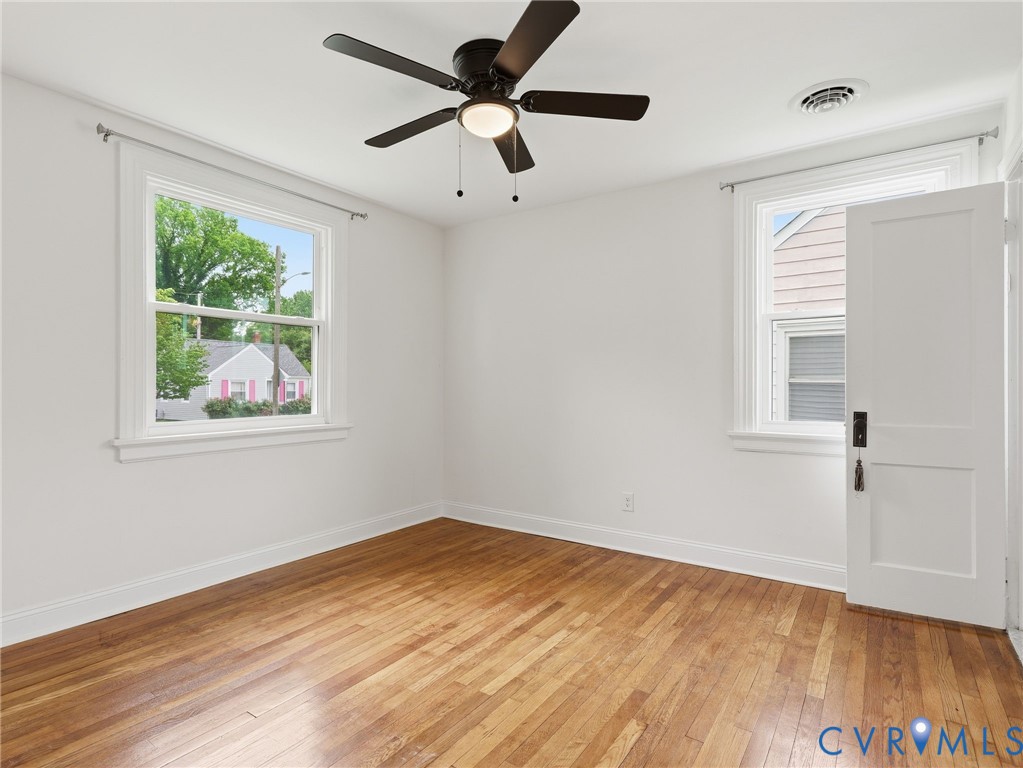 Hardwood flooring throughout this room, featuring two windows with white trim, a white paneled door, and a ceiling fan with light fixture Hardwood flooring throughout this room, featuring two windows with white trim, a white paneled door, and a ceiling fan with light fixture