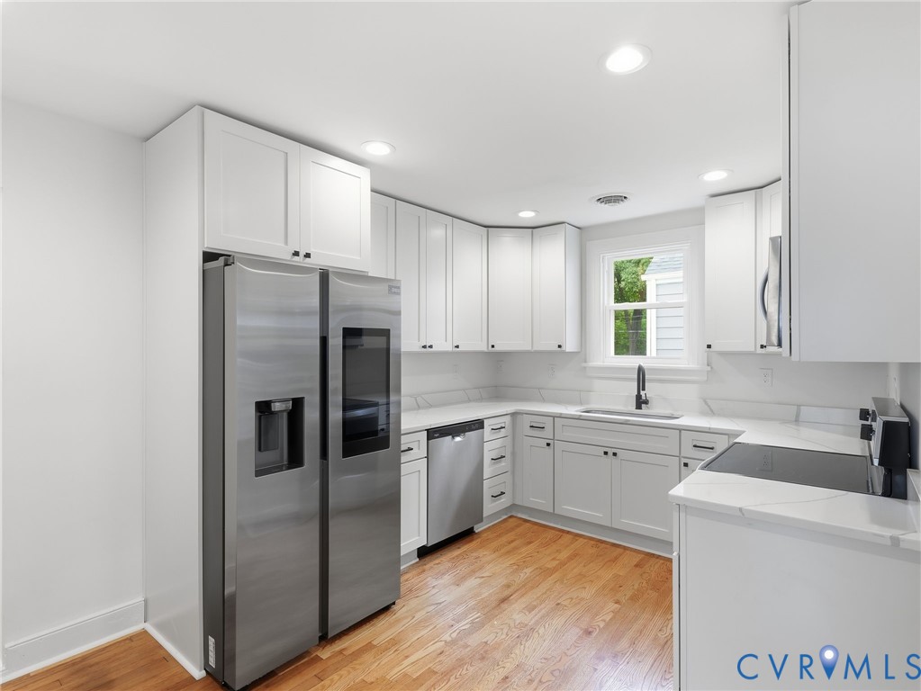 Modern kitchen featuring white shaker cabinetry, stainless steel appliances, light-toned countertops with a matching backsplash, recessed lighting, and wood-finish flooring Modern kitchen featuring white shaker cabinetry, stainless steel appliances, light-toned countertops with a matching backsplash, recessed lighting, and wood-finish flooring