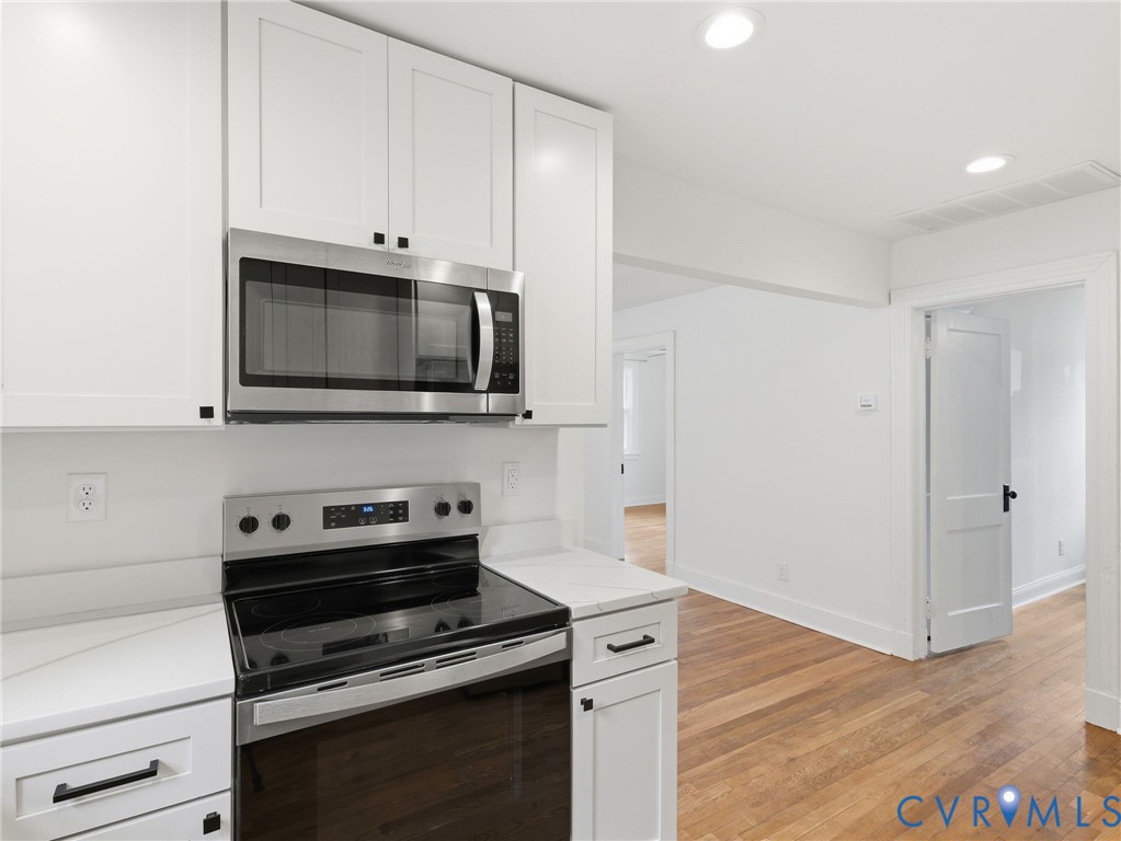 Kitchen featuring white shaker cabinetry, stainless steel microwave, stainless steel electric range, and light-toned countertops Kitchen featuring white shaker cabinetry, stainless steel microwave, stainless steel electric range, and light-toned countertops