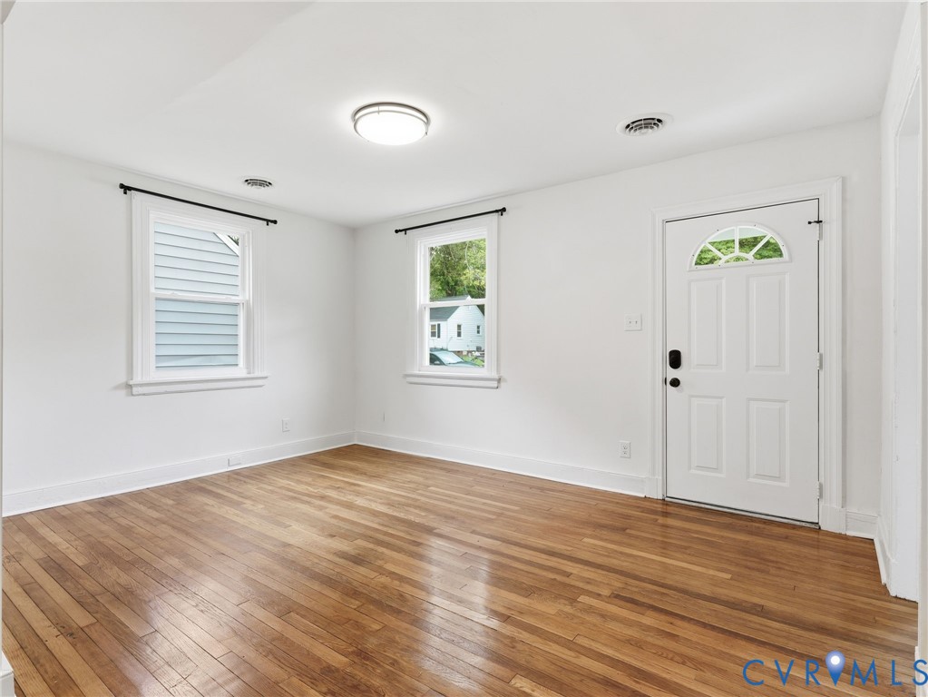 Interior room featuring wood-finish flooring, white walls, and a white paneled door with an arched window insert Interior room featuring wood-finish flooring, white walls, and a white paneled door with an arched window insert