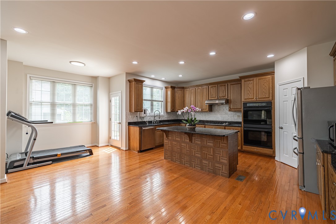 Kitchen featuring wood-finish flooring, recessed lighting, and a central island with a dark countertop Kitchen featuring wood-finish flooring, recessed lighting, and a central island with a dark countertop