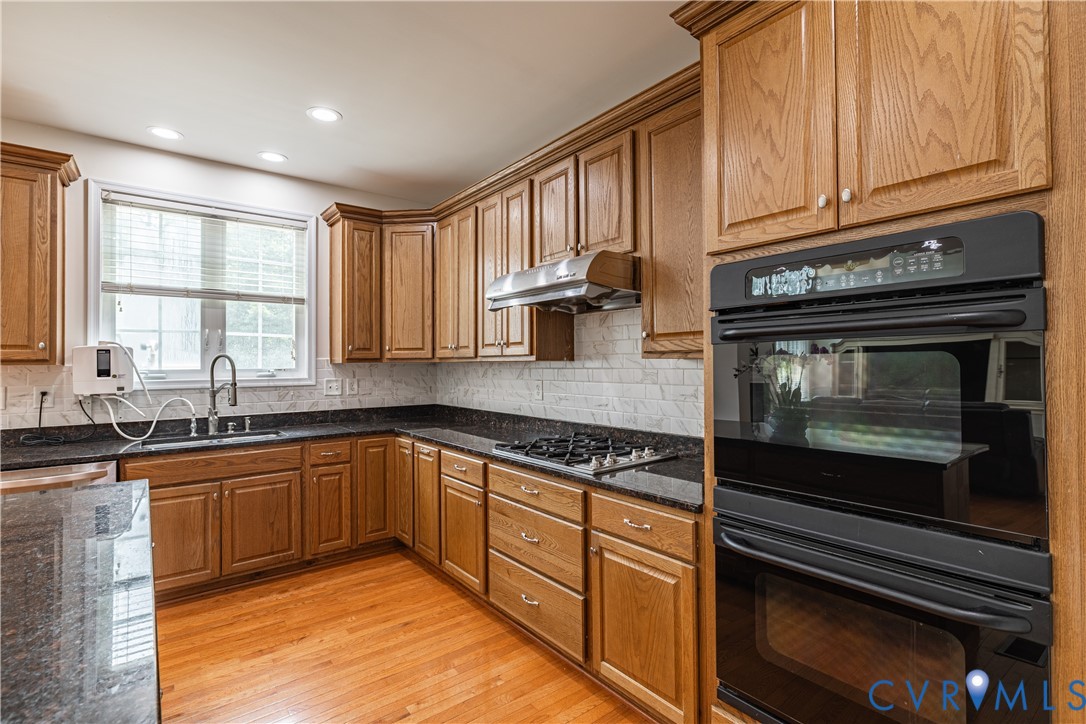 Kitchen featuring wood cabinetry, dark countertops, a tile backsplash, and wood-finish flooring