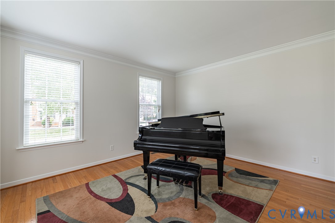 Bright room featuring hardwood flooring, white walls, two double-hung windows with blinds, and white crown molding