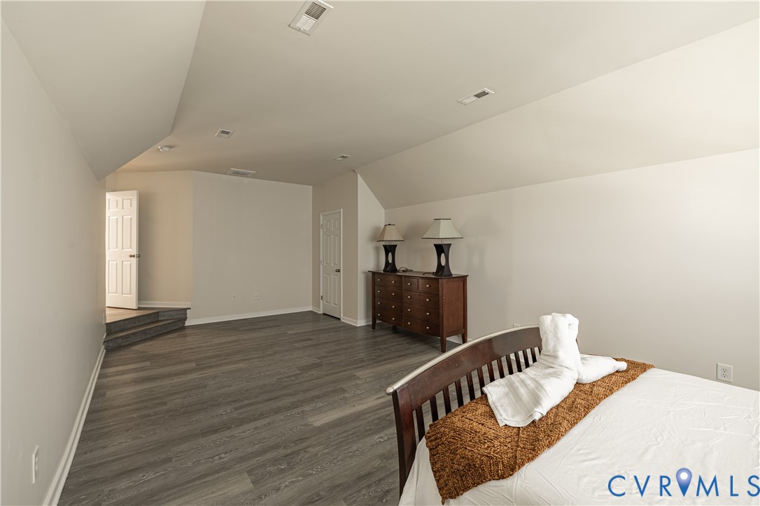 Spacious room featuring vaulted ceilings, recessed lighting, wood-finish flooring, white trim, and a white paneled door