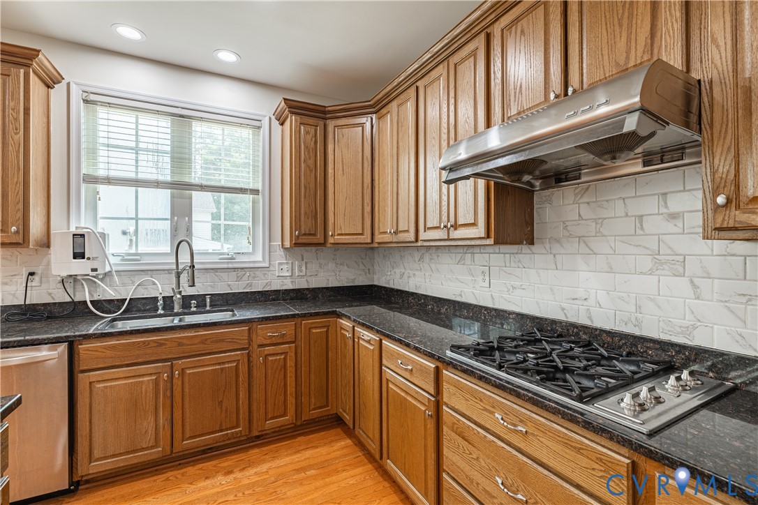 Kitchen featuring wood cabinetry, dark countertops, a stainless steel gas cooktop, a stainless steel range hood, and a subway tile backsplash