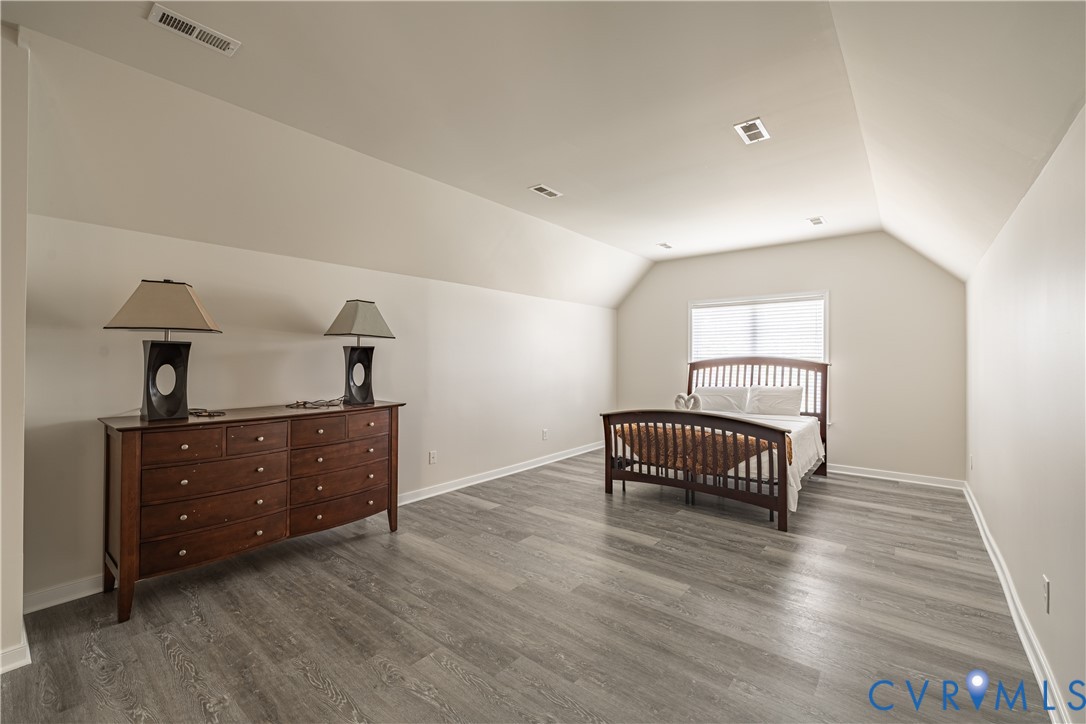 Spacious room featuring vaulted ceilings, a window with blinds, recessed lighting, and wood-finish flooring