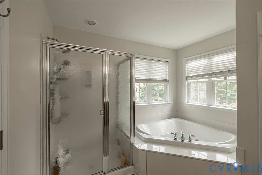 Corner soaking tub with deck-mounted chrome fixtures, surrounded by a tiled wall and two windows