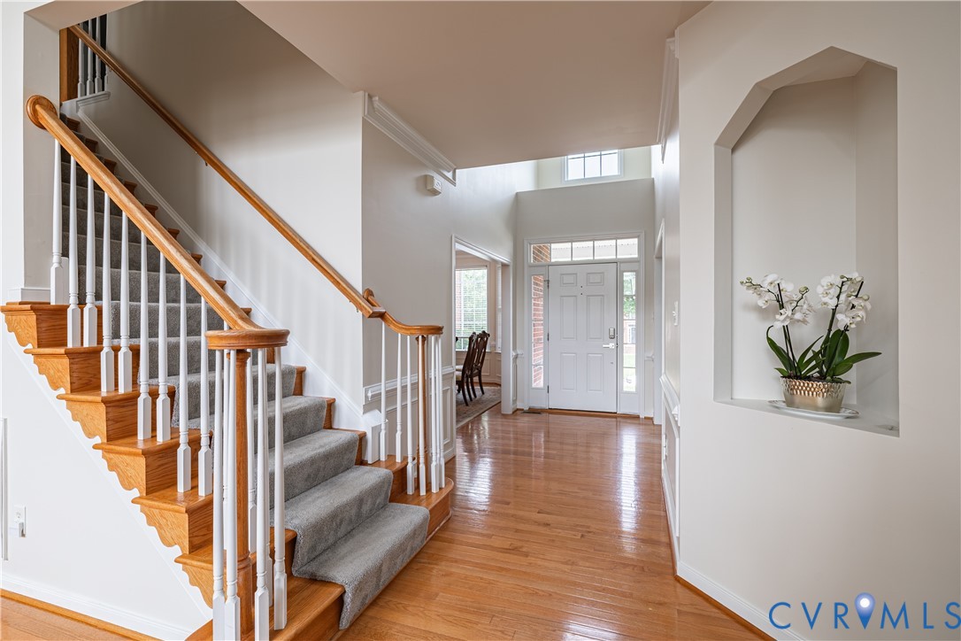 Bright foyer with wood-finish flooring, a grand staircase with wood handrails, and a decorative wall niche Bright foyer with wood-finish flooring, a grand staircase with wood handrails, and a decorative wall niche