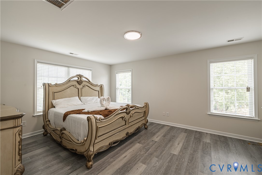Spacious room featuring wood-finish flooring, light-toned walls, and multiple windows with blinds