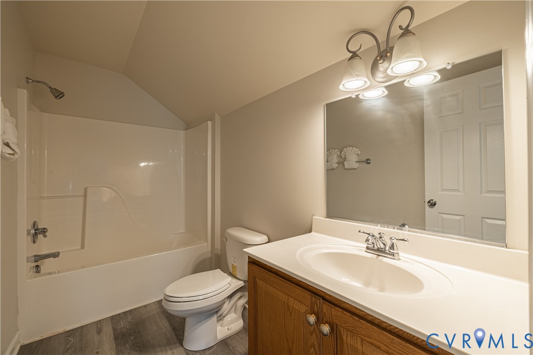 Bathroom featuring a white tub-shower combination, a toilet, and a vanity with a white countertop and wood-finish cabinetry