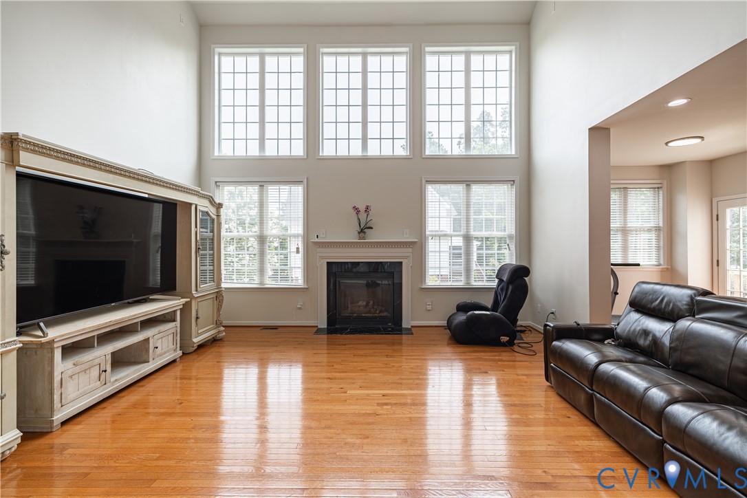 Two-story living area featuring wood-finish flooring, a fireplace with a mantel, and multiple windows Two-story living area featuring wood-finish flooring, a fireplace with a mantel, and multiple windows