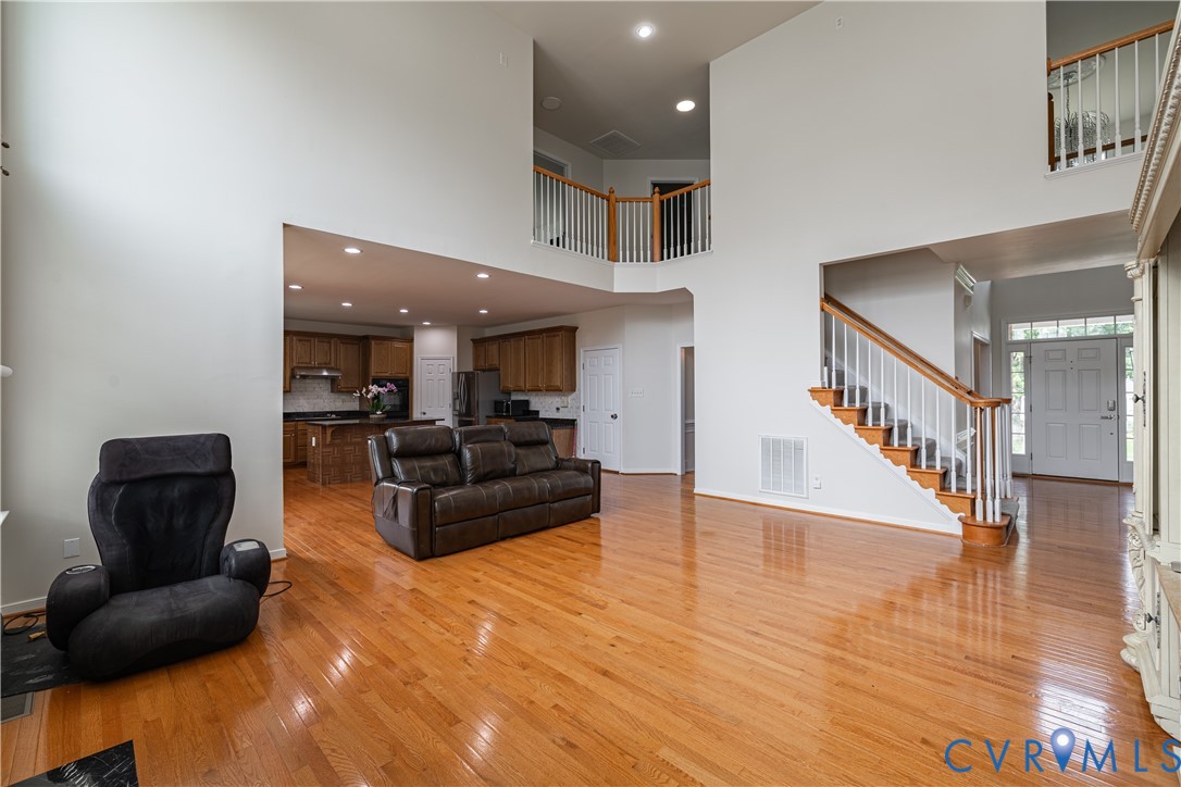 Two-story living area featuring wood-finish flooring, a grand staircase with white balusters and wood handrails, and an open concept layout to the kitchen Two-story living area featuring wood-finish flooring, a grand staircase with white balusters and wood handrails, and an open concept layout to the kitchen
