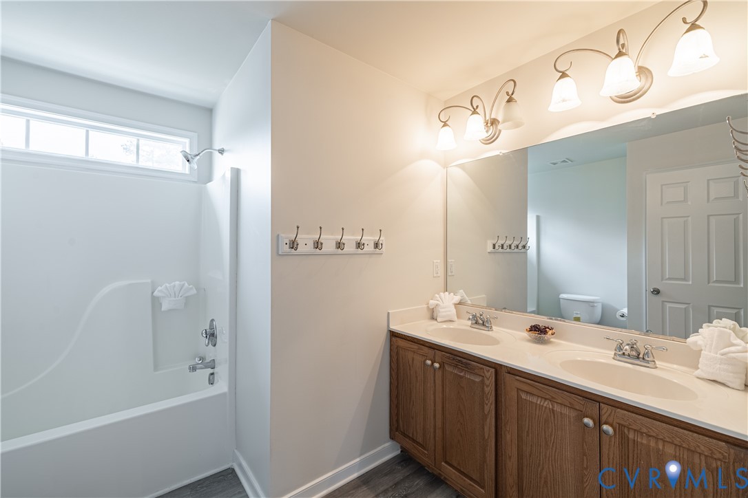 Bathroom featuring a double vanity with wood-finish cabinetry and light-toned countertops, a large vanity mirror, and overhead sconce lighting