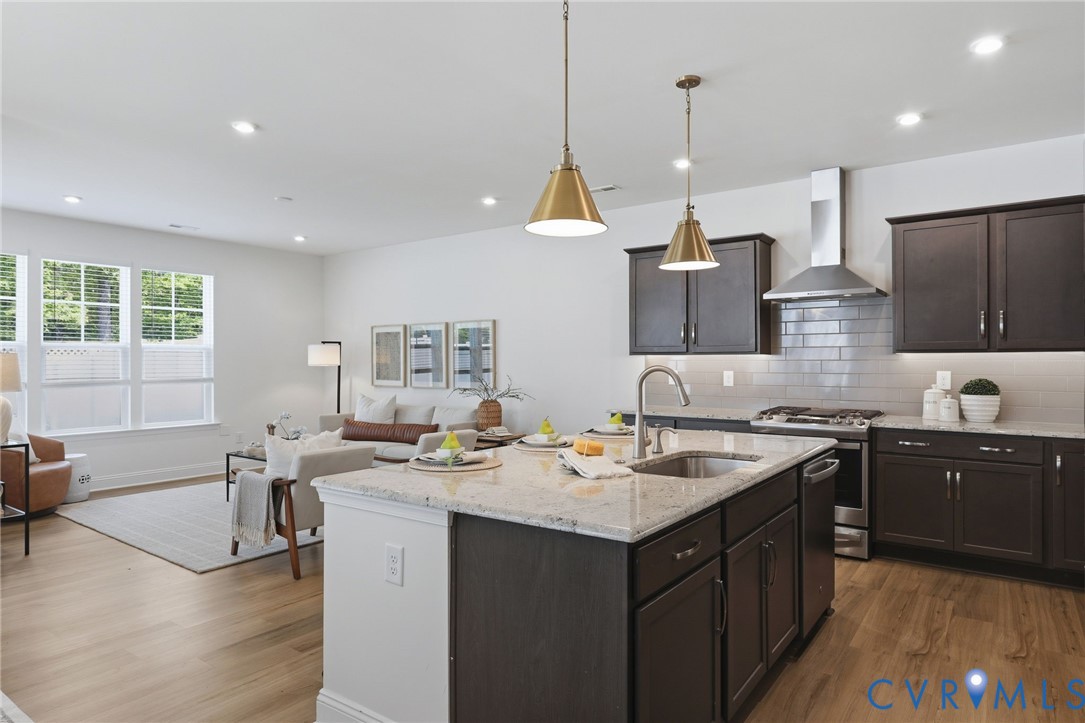 Open-concept living space featuring a kitchen island with stone countertop, stainless steel appliances, dark wood-finish cabinetry, and wood-finish flooring