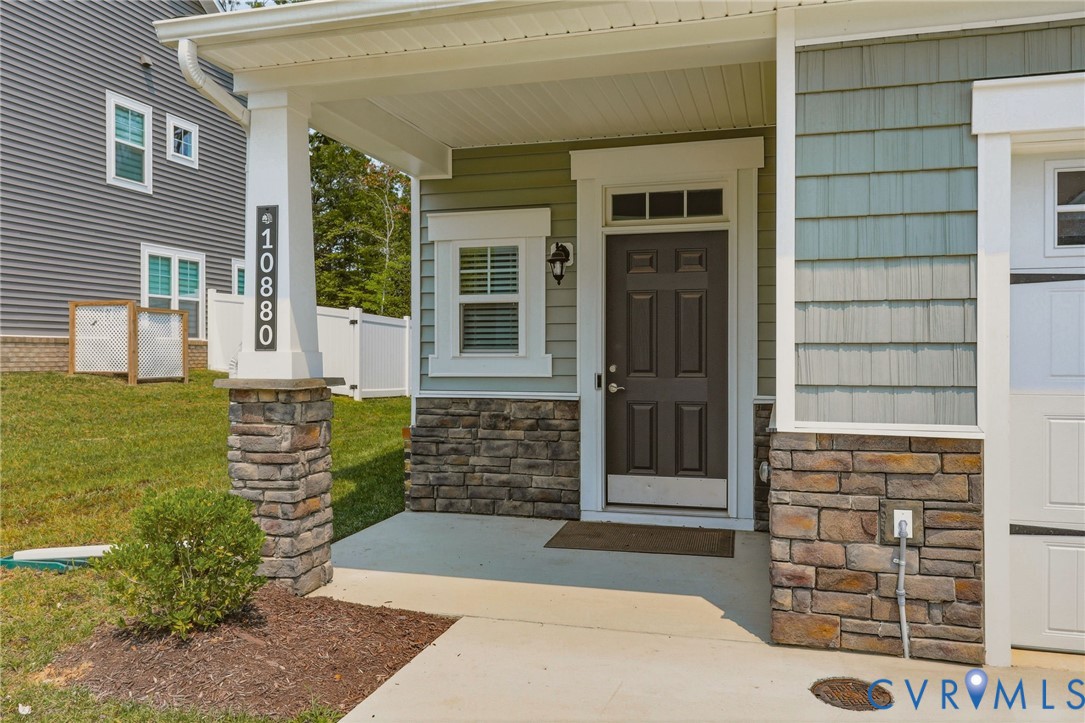 Covered front porch featuring stacked stone accents, vinyl shake siding, and a dark paneled entry door with transom window