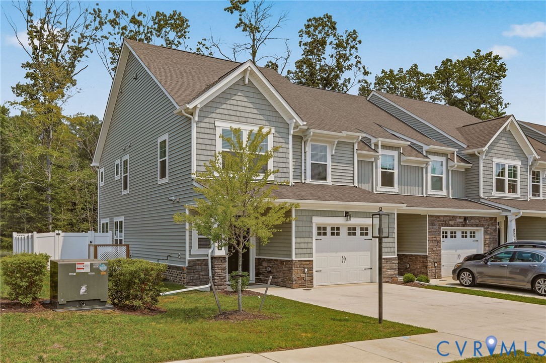 Multi-story townhome featuring grey siding, shake shingles, and stone veneer accents