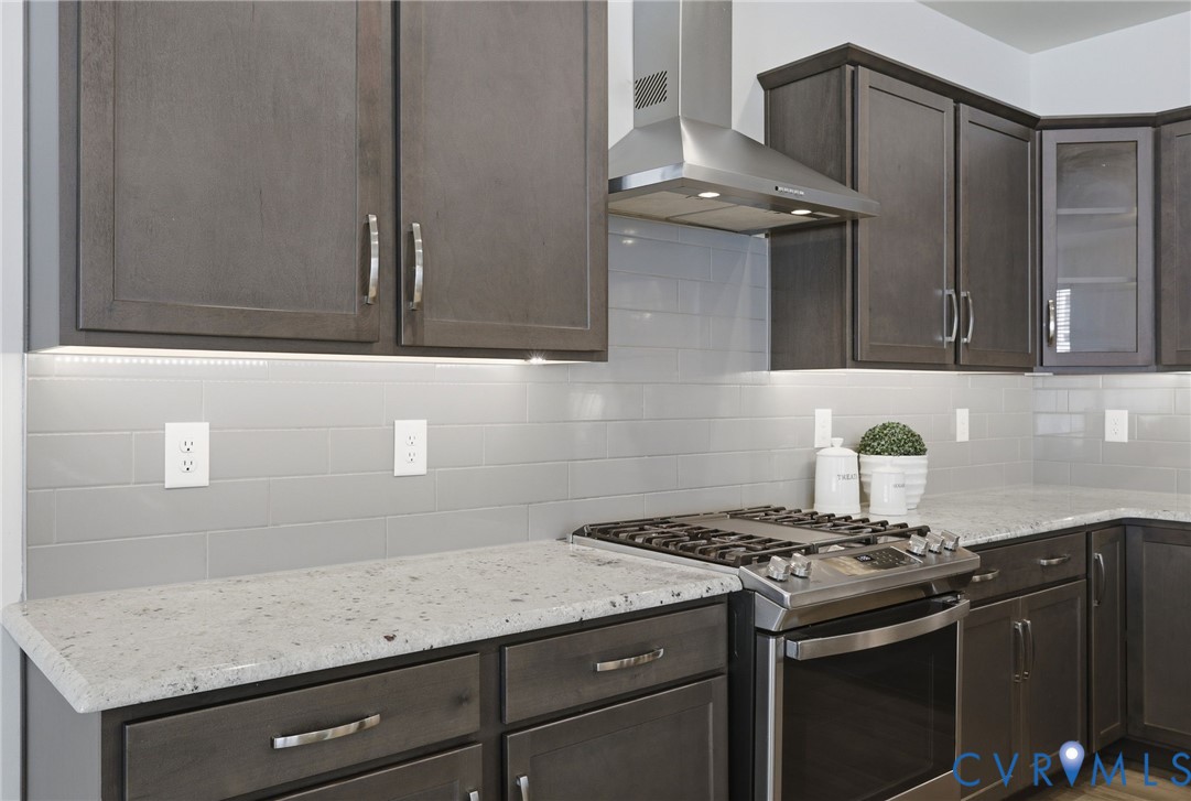 Kitchen featuring dark wood cabinetry, light-toned countertops, a stainless steel gas range, and a coordinating stainless steel range hood