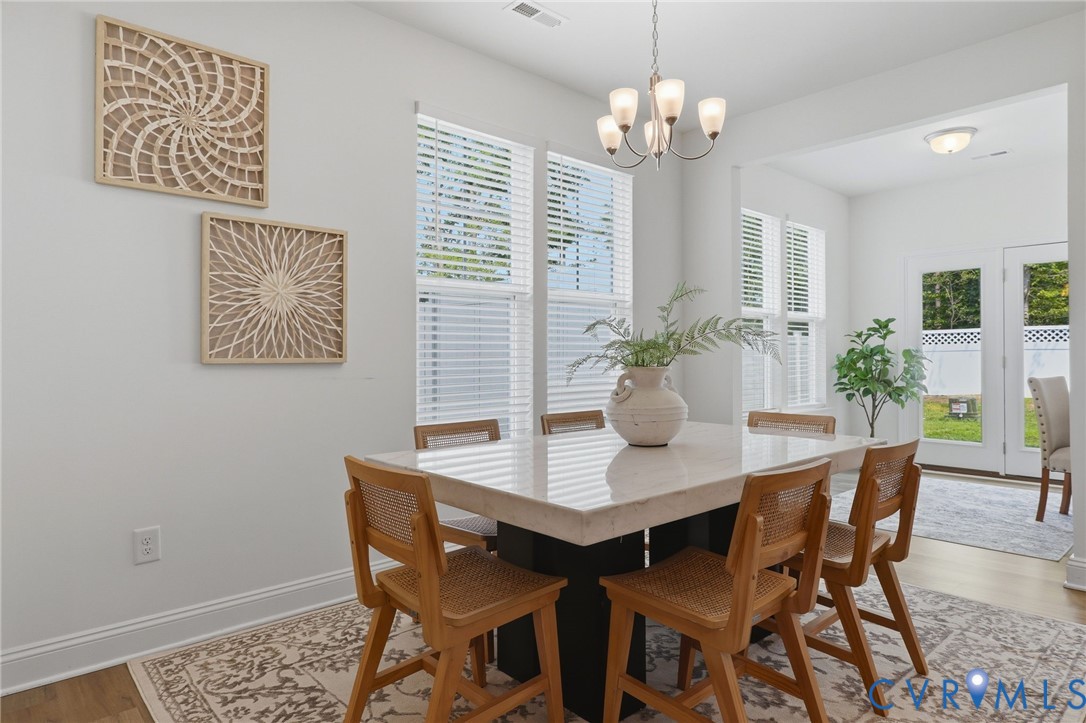 Bright interior space featuring a multi-light chandelier, multiple windows with blinds, and light wood-finish flooring
