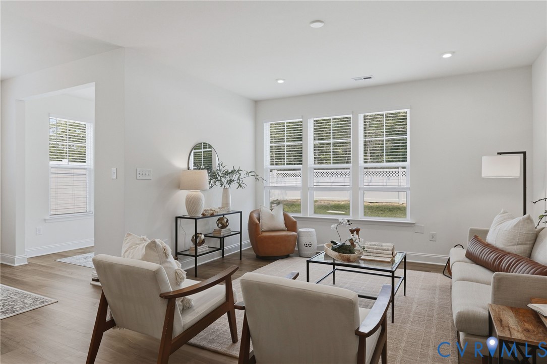 Bright living space featuring multiple windows with blinds, recessed lighting, wood-finish flooring, and white baseboards