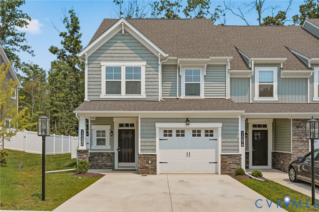 Modern townhome exterior featuring light blue siding, stone accents, a single-car garage, and a front entry door with transom window Modern townhome exterior featuring light blue siding, stone accents, a single-car garage, and a front entry door with transom window