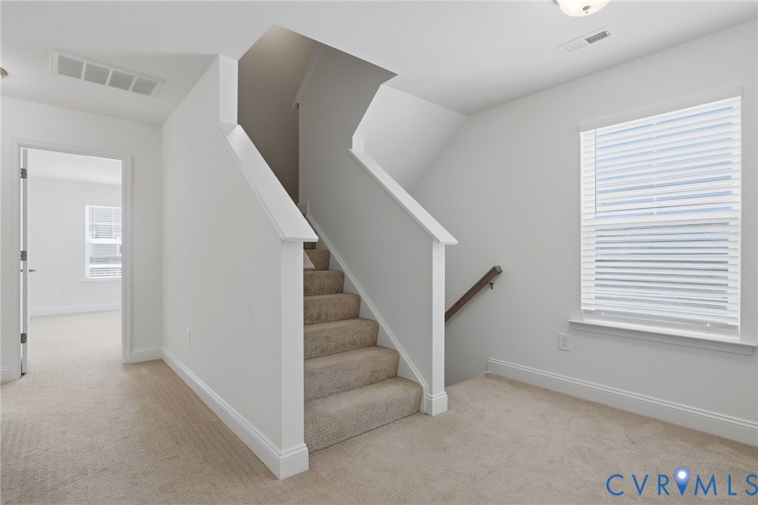 Carpeted staircase with white balustrade, window with blinds, and neutral wall paint