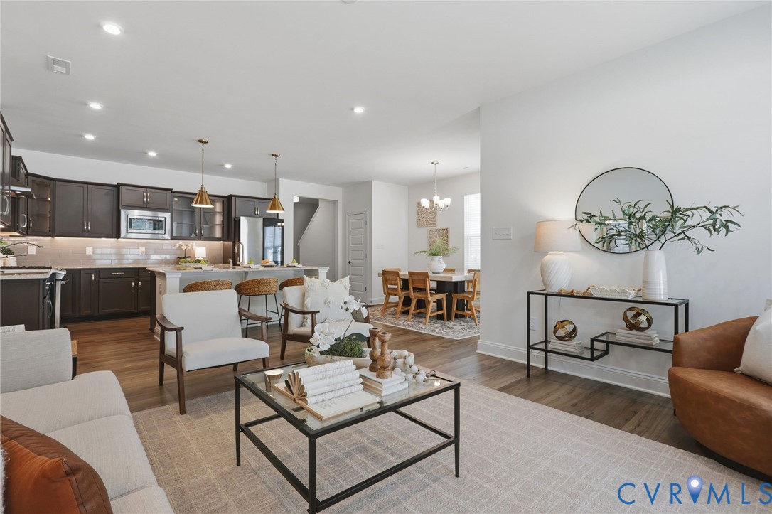 Open-concept living area featuring wood-finish flooring, recessed lighting, and a kitchen with dark cabinetry, stainless steel appliances, and a light-toned island with pendant lighting