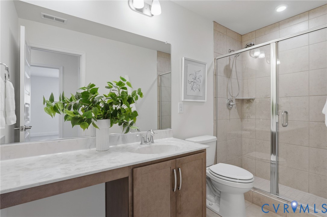 Bathroom featuring a wood-finish vanity with an integrated sink, a large mirror, and a tiled shower with a glass enclosure