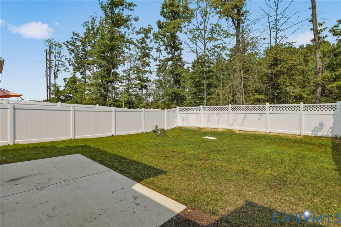 Expansive grassy yard featuring a concrete patio, full white vinyl fencing with lattice accents, and mature perimeter trees