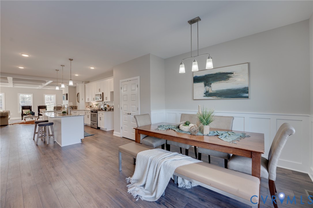 Open-concept interior featuring wood-finish flooring, white wainscoting, and a linear pendant light fixture