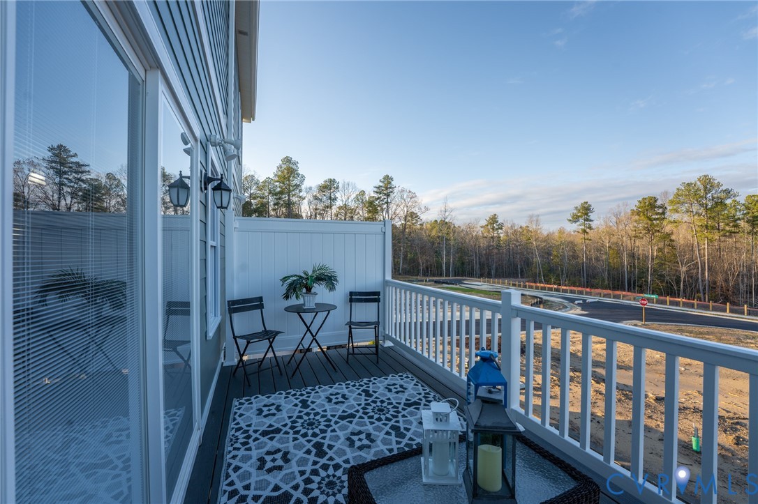 Private balcony featuring composite decking, white railing, and exterior wall lighting