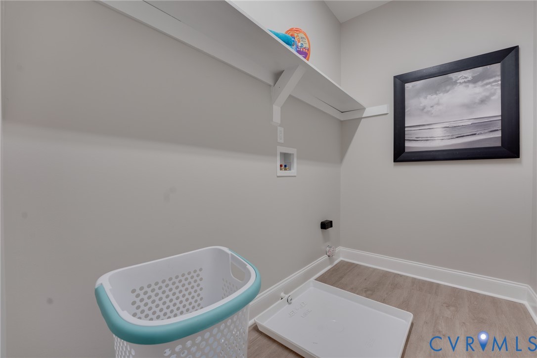 Dedicated laundry area featuring a wall-mounted shelf, light gray wall paint, and wood-finish flooring with white baseboards