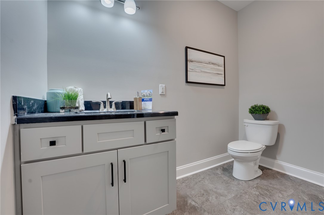 Bathroom featuring a light grey vanity with black hardware, a black countertop, and a white toilet