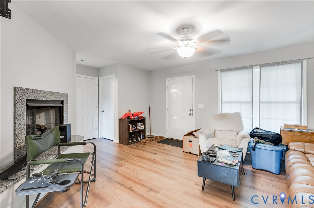 Spacious living area featuring wood-finish flooring, a ceiling fan with integrated lighting, and multiple windows providing natural light Spacious living area featuring wood-finish flooring, a ceiling fan with integrated lighting, and multiple windows providing natural light