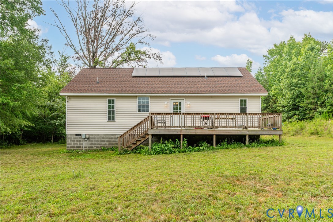 Rear exterior featuring a spacious wood deck with steps, tan vinyl siding, a brown shingle roof, and visible solar panels