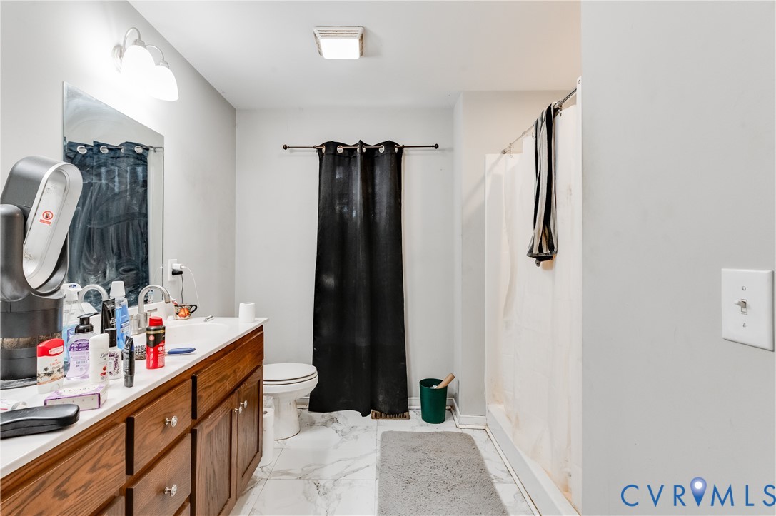 Bathroom featuring a wood-finish vanity with an integrated countertop and sink, a wall-mounted mirror, overhead lighting, and a shower with a white curtain