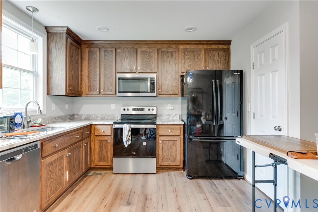 Kitchen featuring wood-finish cabinetry, light-toned countertops, and stainless steel appliances Kitchen featuring wood-finish cabinetry, light-toned countertops, and stainless steel appliances